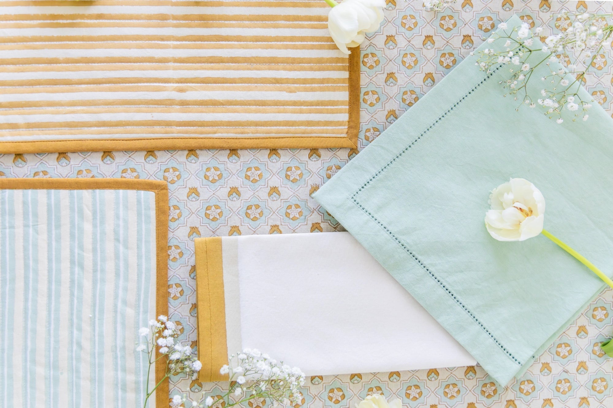 Light green napkin on a floral-patterned tablecloth with wooden placemats and white flowers.