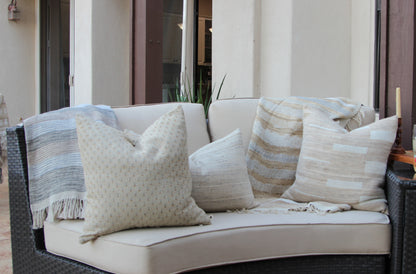 Handwoven striped throw with fringe draped over an outdoor sofa with handwoven cushions in cream, beige and soft blue