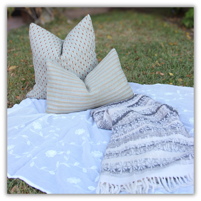Handwoven gray and white floral throw with fringe, styled with a sage hand block printed cushion and a striped cushion on grass